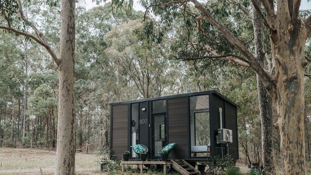 Une petite cabane à l’extérieur sombre, une porte portant le numéro « 800 », deux chaises avec des coussins à motifs et un petit escalier menant à l’entrée.