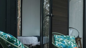 Une terrasse en bois avec deux hamacs verts, un lit et des plantes en pot.