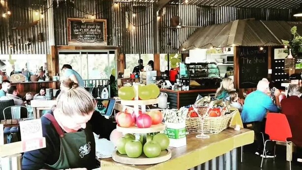 Interior acolhedor de café rústico, com balcão de madeira, cardápio em lousa e área de estar com mesas e cadeiras.
