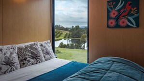 Um quarto com uma cama, uma janela com vista para um lago e um quadro na parede.