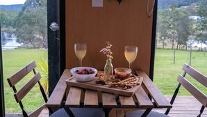 Uma mesa de madeira com uma tigela de frutas, um copo de vinho e um pequeno vaso com flores.