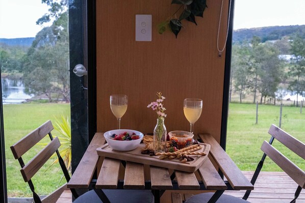 A wooden table with a bowl of fruit, a glass of wine, and a small vase with flowers.