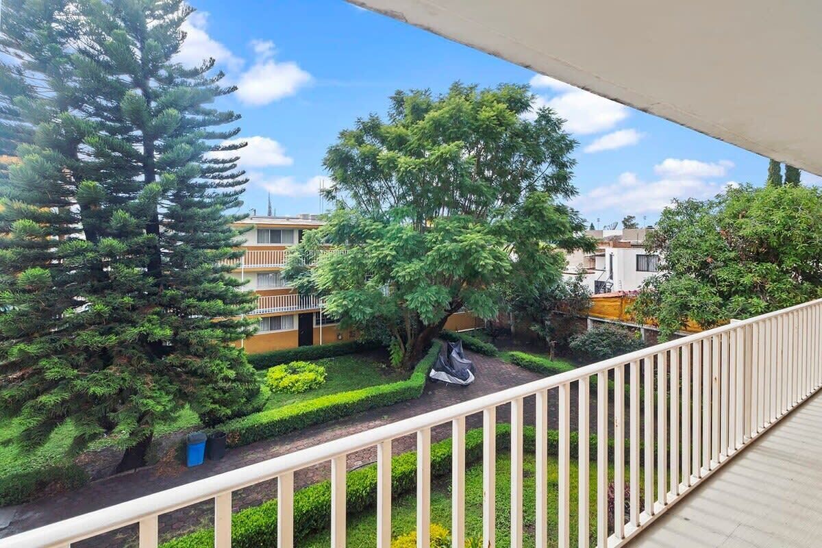 A balcony with a view of a well-maintained garden, including a large tree and neatly trimmed bushes.