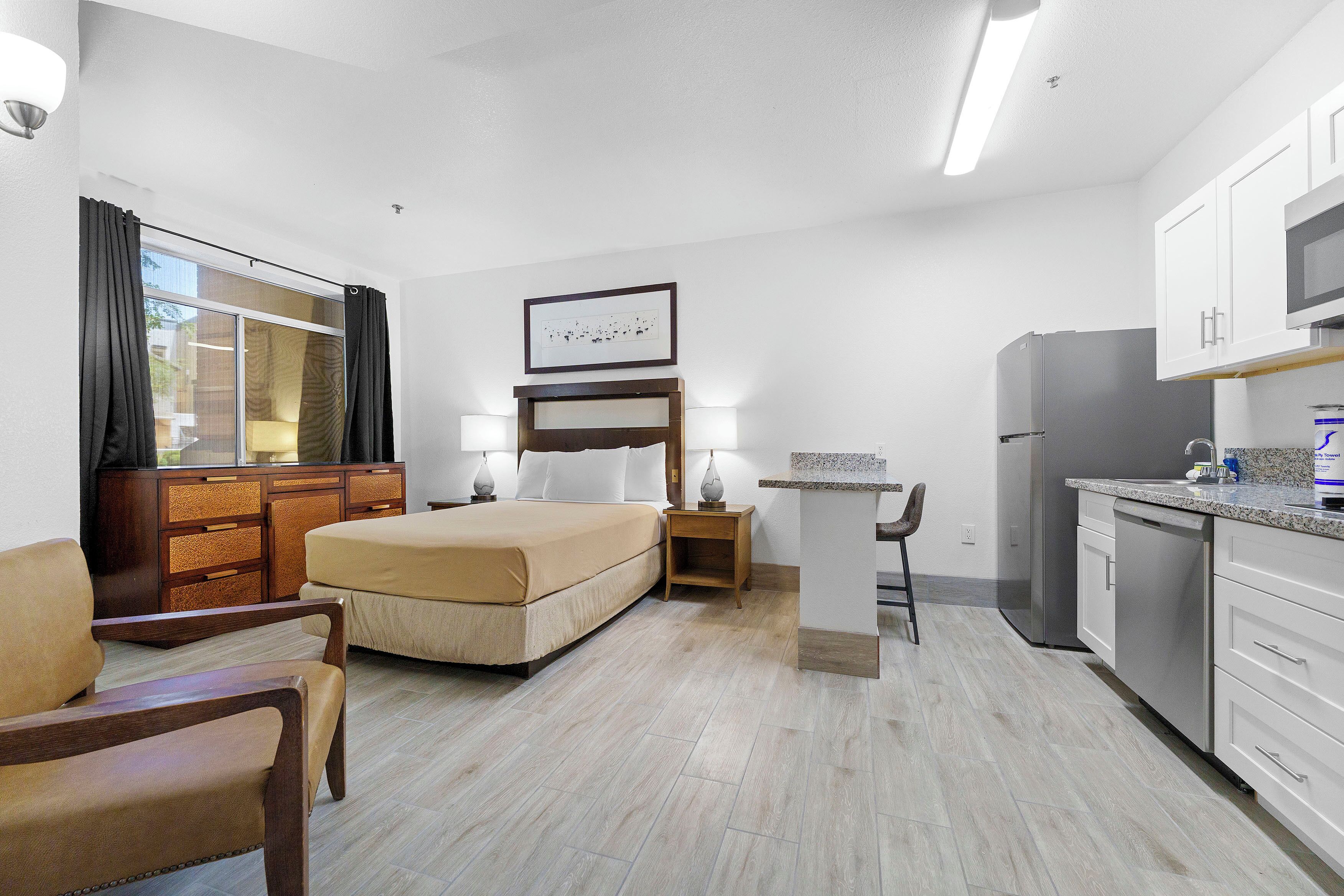 Quarto de hotel com cama, escrivaninha, cadeira, guarda-roupa, frigorífico e micro-ondas.