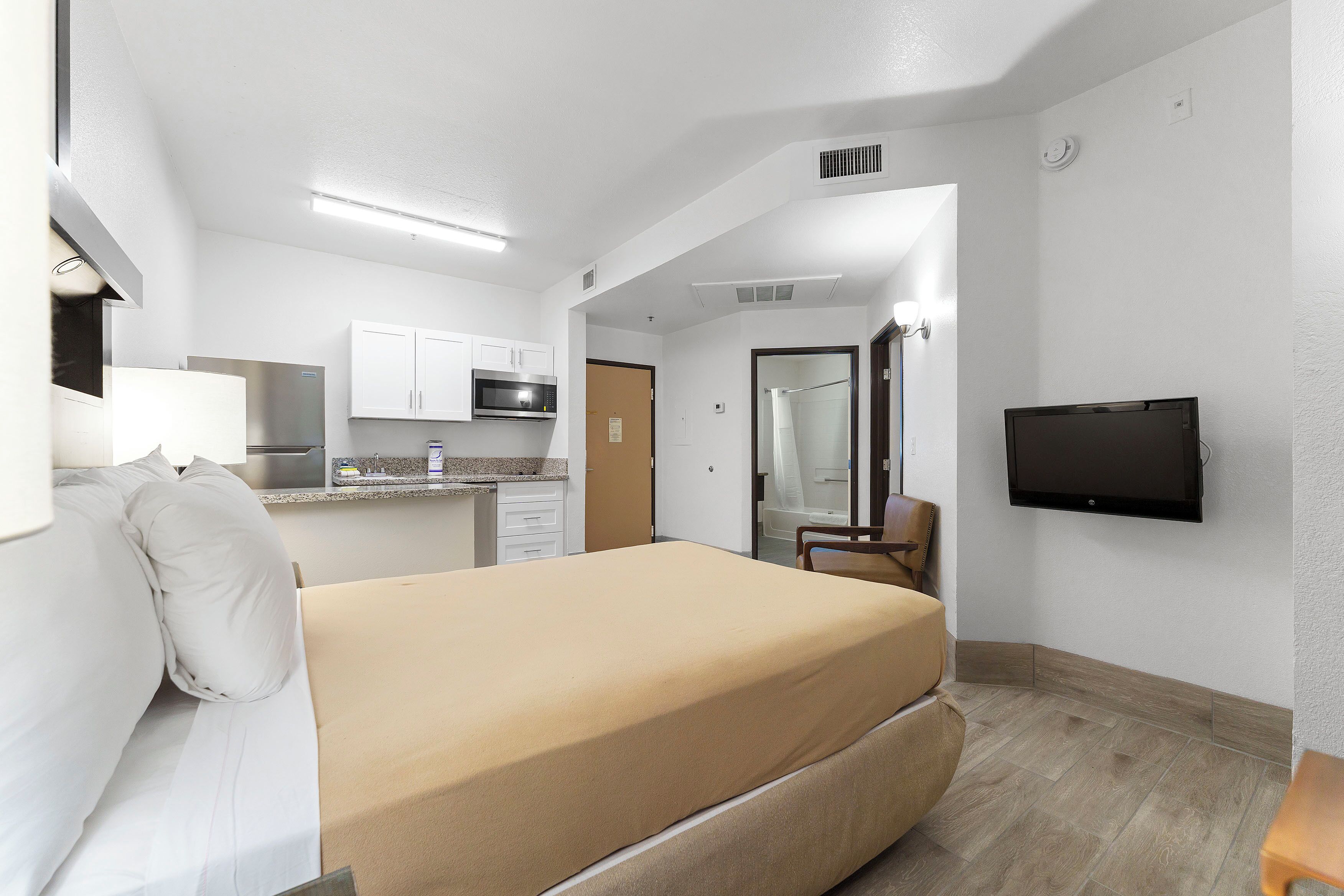 A hotel room with a bed, a TV, a kitchenette, and a bathroom.