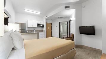 A hotel room with a bed, a TV, a kitchenette, and a bathroom.