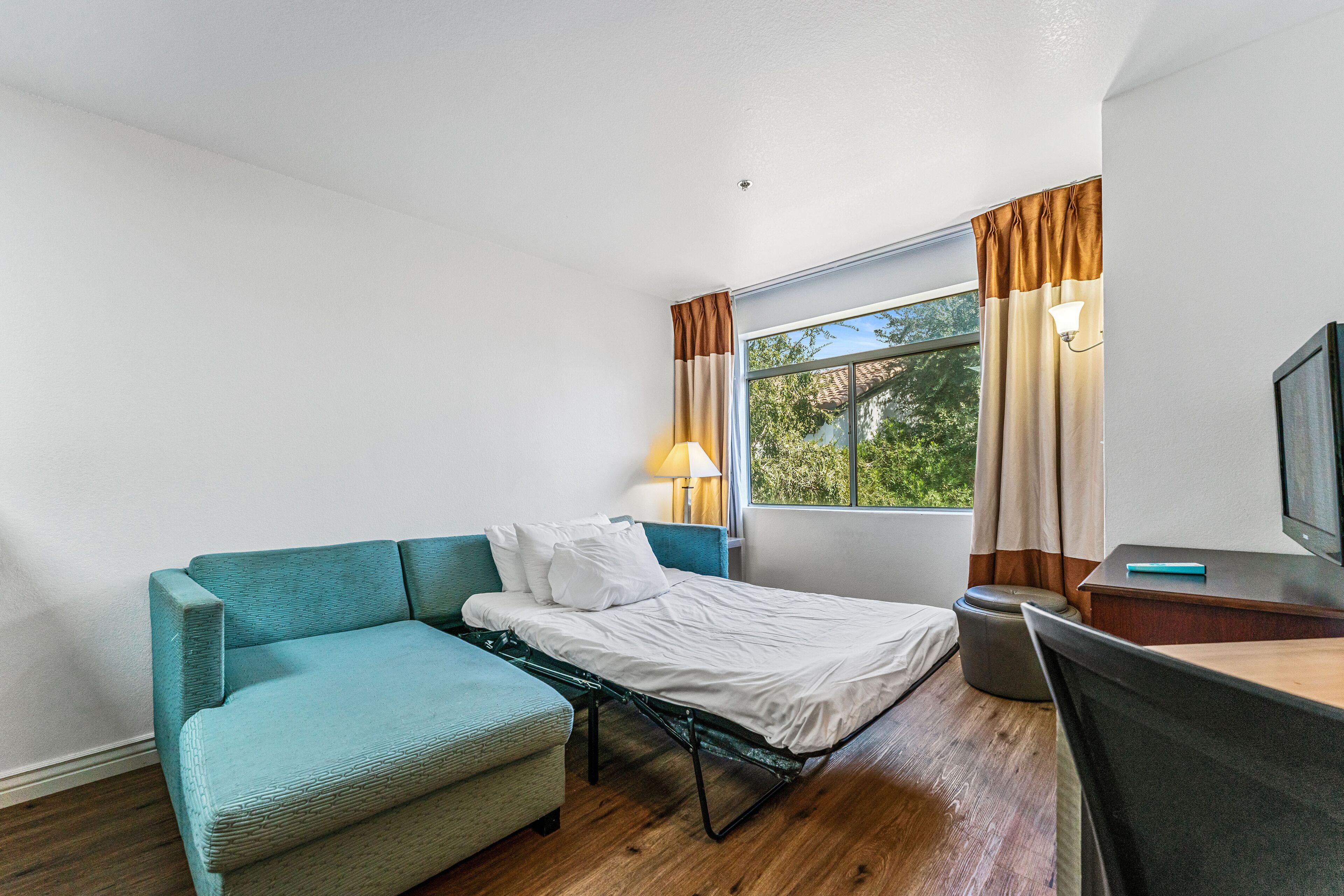 A compact room with a bed, a sofa, a desk, and a window with curtains.