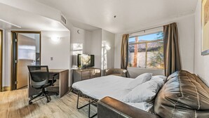 Habitación de hotel con cama, escritorio, silla, televisor y ventana con cortinas.
