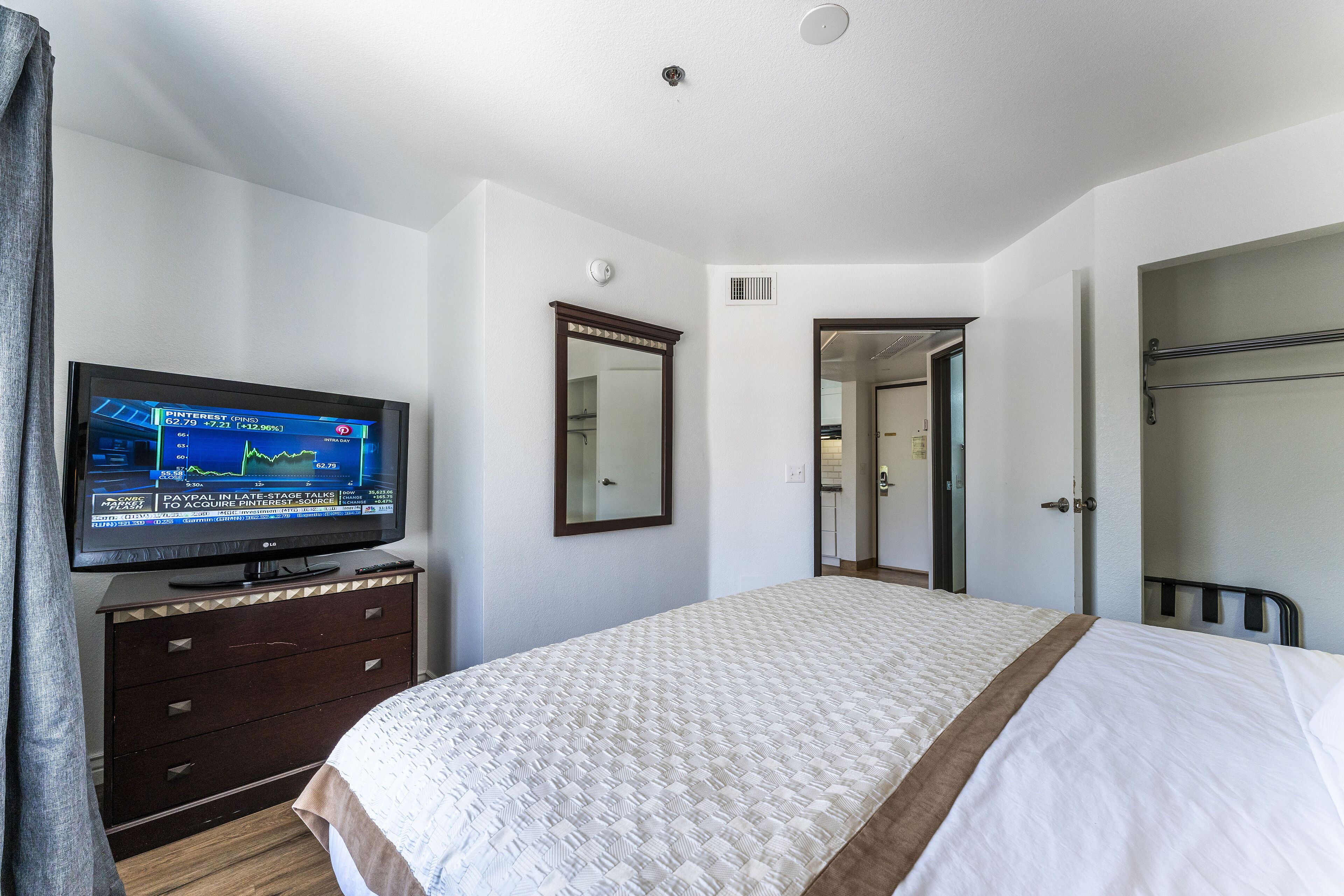 Une chambre d’hôtel avec un lit, un téléviseur posé sur une commode, un miroir et une porte donnant sur une autre pièce.