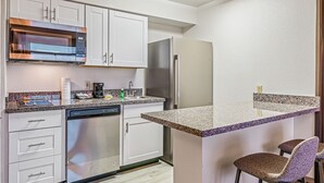 Una cocina moderna con armarios blancos, un microondas de acero inoxidable, refrigerador y lavavajillas.