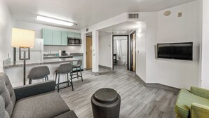 A modern kitchen with a microwave, refrigerator, and bar stools. There is a living area with a sofa and a TV mounted on the wall. - Metro Chandler Extended Stay (Chandler)