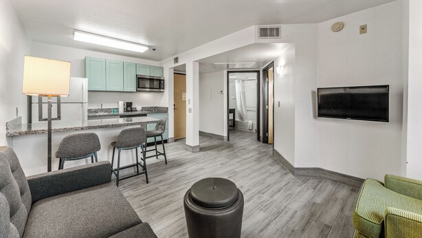 Una cocina moderna con microondas, refrigerador y taburetes de bar. Hay una sala de estar con sofá y televisor montado en la pared.