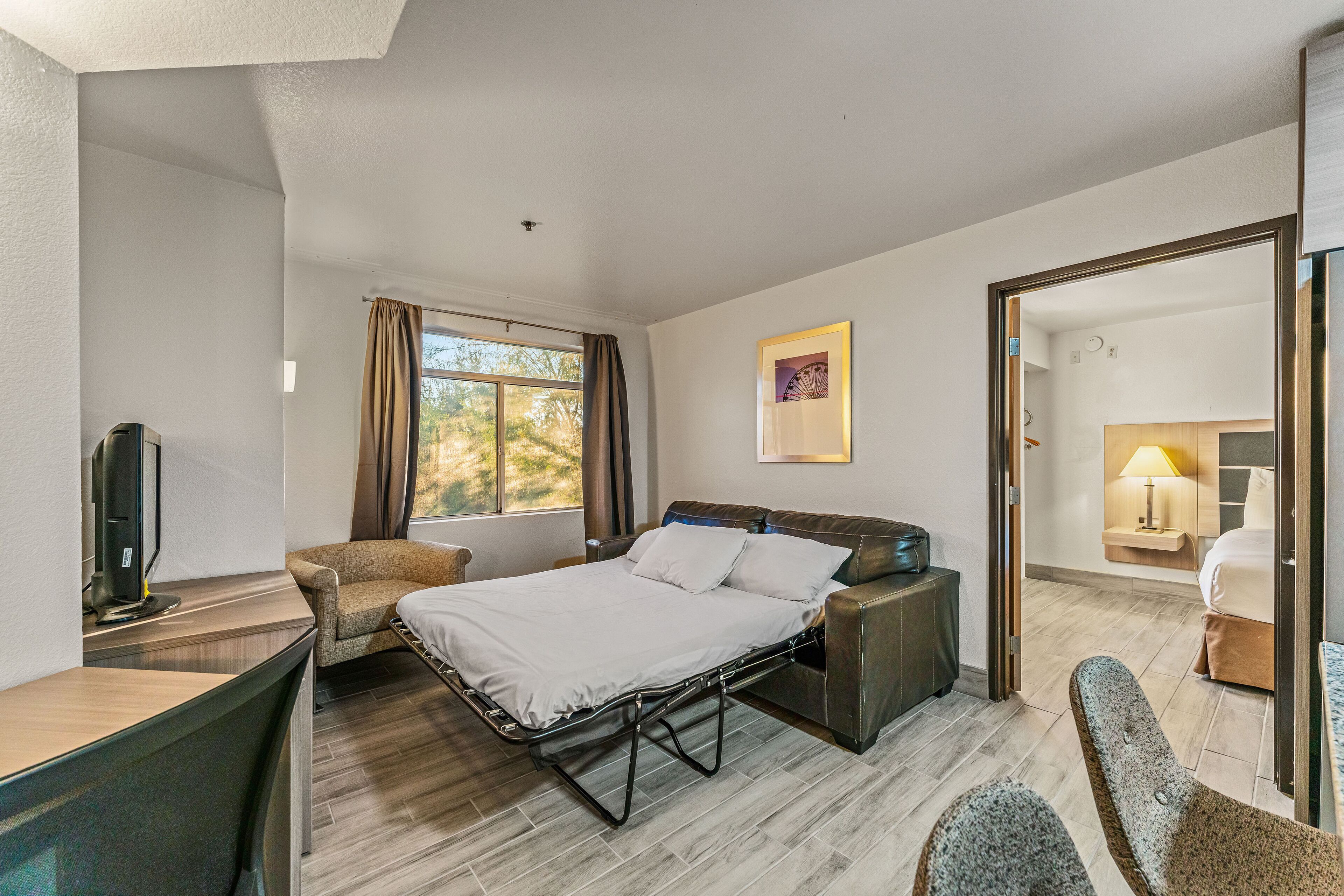 Ein modernes Hotelzimmer mit Bett, Schreibtisch, Stuhl, Fernseher und einem Fenster mit Vorhängen.