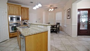 A kitchen with granite countertops, stainless steel appliances, wooden cabinets, a dining area with a table and chairs, and a ceiling fan. - 4 Bedrooms Luxury  Location-  Houston River Oaks (Houston)