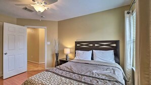 A bedroom with a bed, a nightstand, a lamp, a ceiling fan, and a door leading to another room. - 4 Bedrooms Luxury  Location-  Houston River Oaks (Houston)