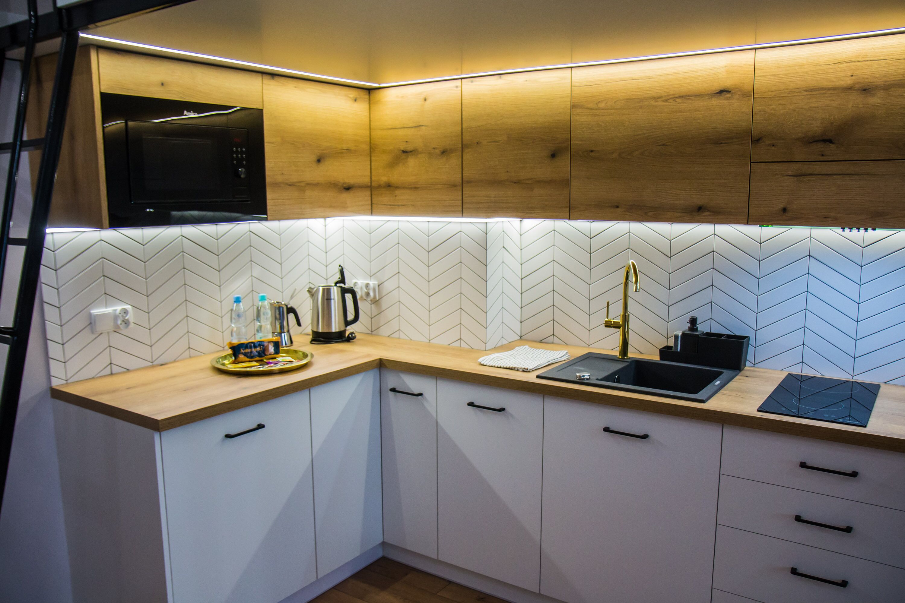 A modern kitchen with wooden cabinets, a microwave, a sink, and a herringbone-patterned backsplash.