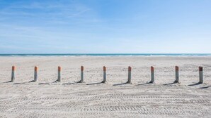 A sandy beach with a row of orange and grey bollards. - "Coastal Vibes" One Block from Beach-Unit 1011-Island Dunes Condominiums (Port Aransas)