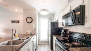 A modern kitchen with stainless steel appliances, a granite countertop, and a visible clock on the wall. - "Coastal Vibes" One Block from Beach-Unit 1011-Island Dunes Condominiums (Port Aransas)