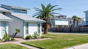 A residential area with houses featuring a light blue exterior, a wooden fence, and a palm tree. - "Coastal Vibes" One Block from Beach-Unit 1011-Island Dunes Condominiums (Port Aransas)