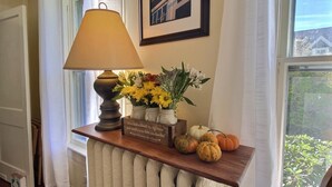 A room with a radiator, a lamp, a framed quote, a vase with flowers, and pumpkins on a shelf. - Historic Colonial...Close to Village Green (Litchfield)