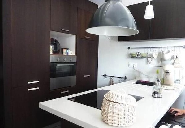Una cocina moderna con armarios de madera oscura, encimera blanca y una lámpara colgante grande.
