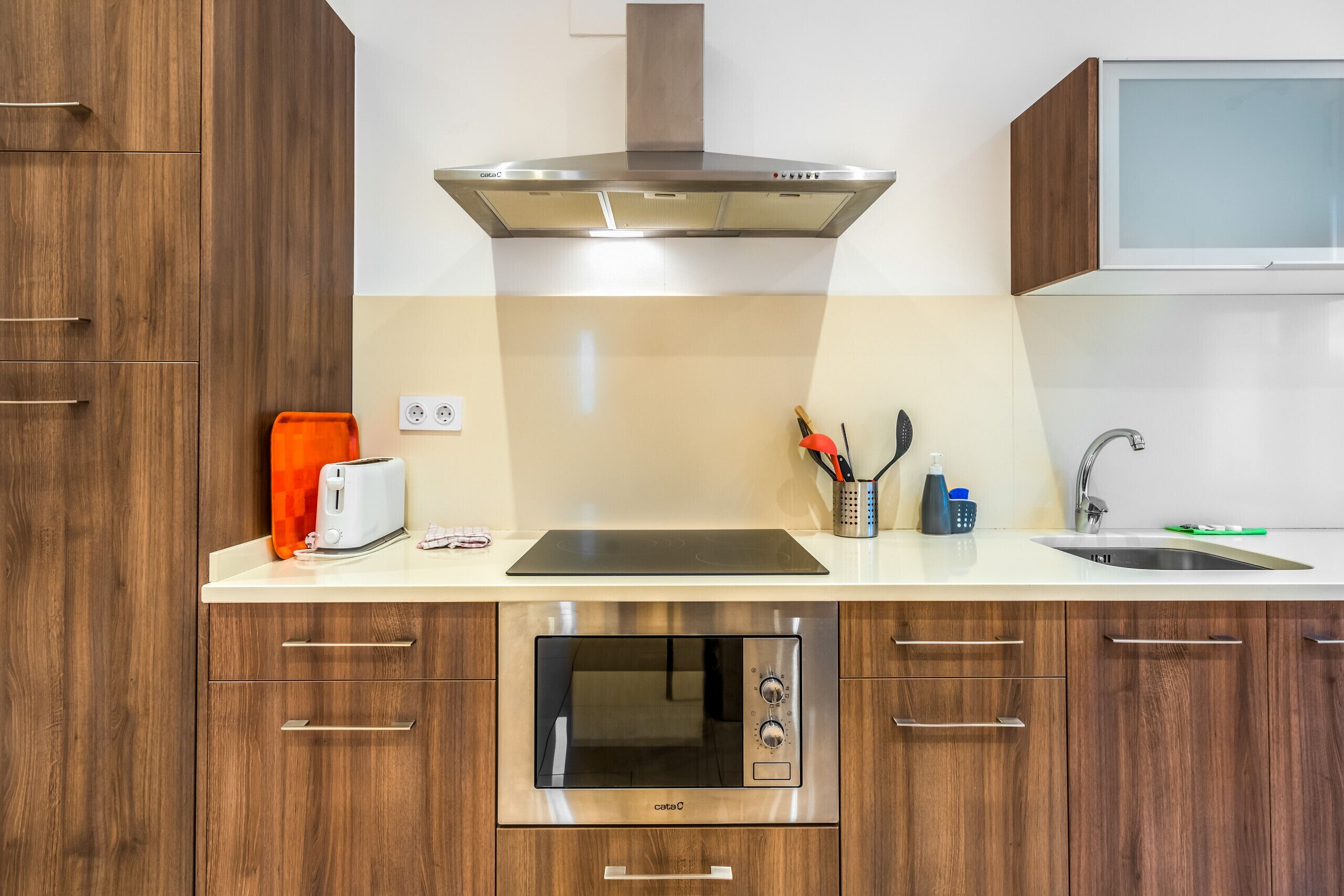 A modern kitchen with wooden cabinets, a built-in oven, a toaster, and a stainless steel range hood.