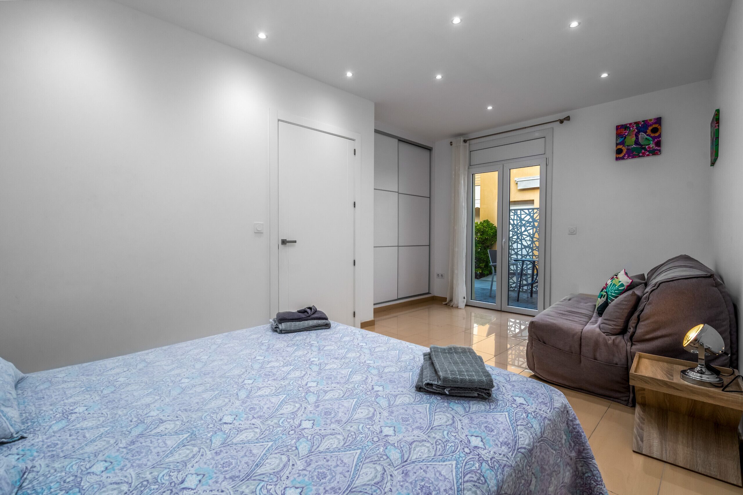 Un dormitorio con cama, sofá, mesita de noche, puerta y vista al exterior.