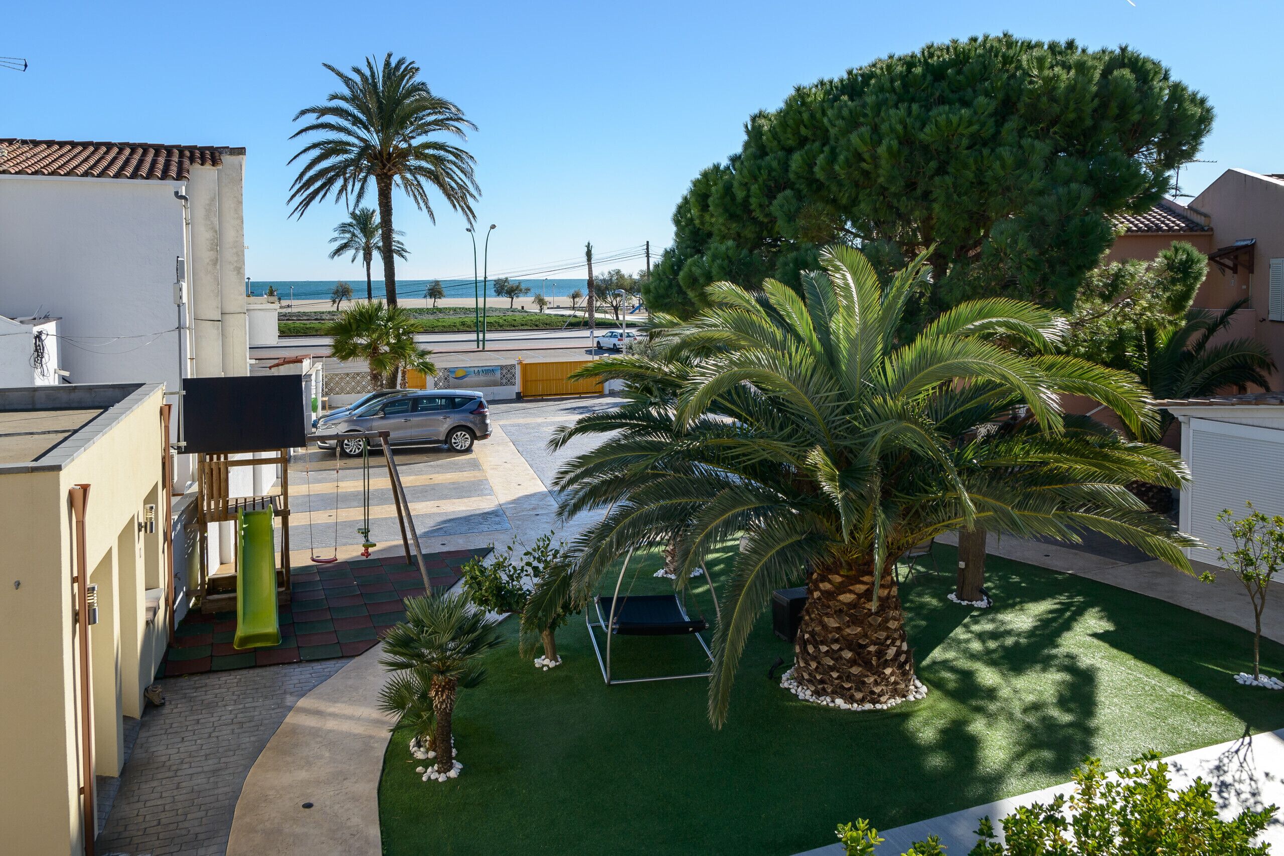Un quartier résidentiel doté d’un terrain de jeux, de palmiers et offrant une vue sur la plage.
