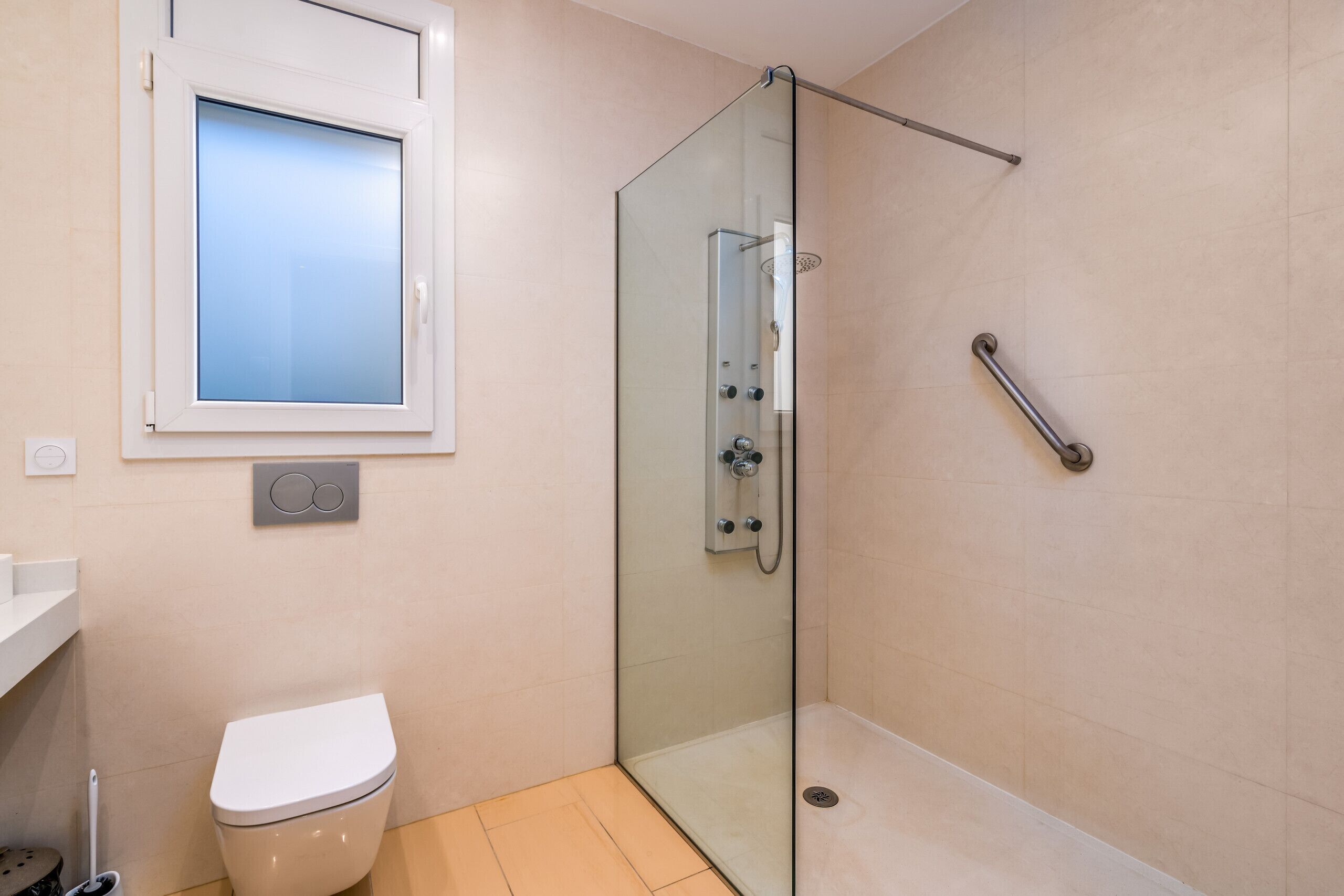 Un baño moderno con ducha de vidrio, inodoro y ventana.