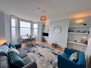 Una sala de estar moderna con comedor, ventanas amplias, un espejo redondo y estanterías empotradas.