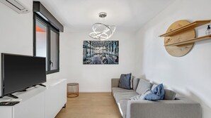 Uma sala de estar moderna com televisão de tela plana, um sofá cinza, piso de madeira e um grande quadro abstrato na parede.