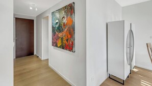 Um corredor com área de cozinha moderna, apresentando uma geladeira branca e um quadro abstrato colorido na parede.
