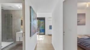 Um interior moderno com chuveiro de vidro, um corredor que leva a um quarto e uma grande pintura abstrata.