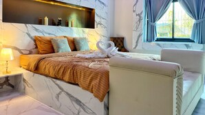 Habitació d'hotel moderna amb paret de marbre, un llit amb mantell marró, una taula de nit amb una làmpada i una finestra amb cortines.