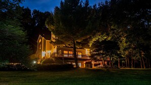 A two-story house with a balcony, surrounded by trees and illuminated by warm lights. - Wow Sunsets/Hot Tub/Fab Game Room/Fire Pit! Close to Owners' Club, Golf and Spa! (Galena)