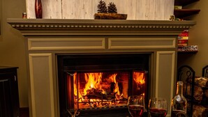 A fireplace with a fire, a table with wine glasses and a bottle, and a shelf with books and a box. - Wow Sunsets/Hot Tub/Fab Game Room/Fire Pit! Close to Owners' Club, Golf and Spa! (Galena)