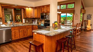 A spacious kitchen with wooden cabinets, granite countertops, and a central island with stools. - Wow Sunsets/Hot Tub/Fab Game Room/Fire Pit! Close to Owners' Club, Golf and Spa! (Galena)