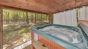 Una cabaña de madera con jacuzzi, ventanas grandes y vistas al bosque.