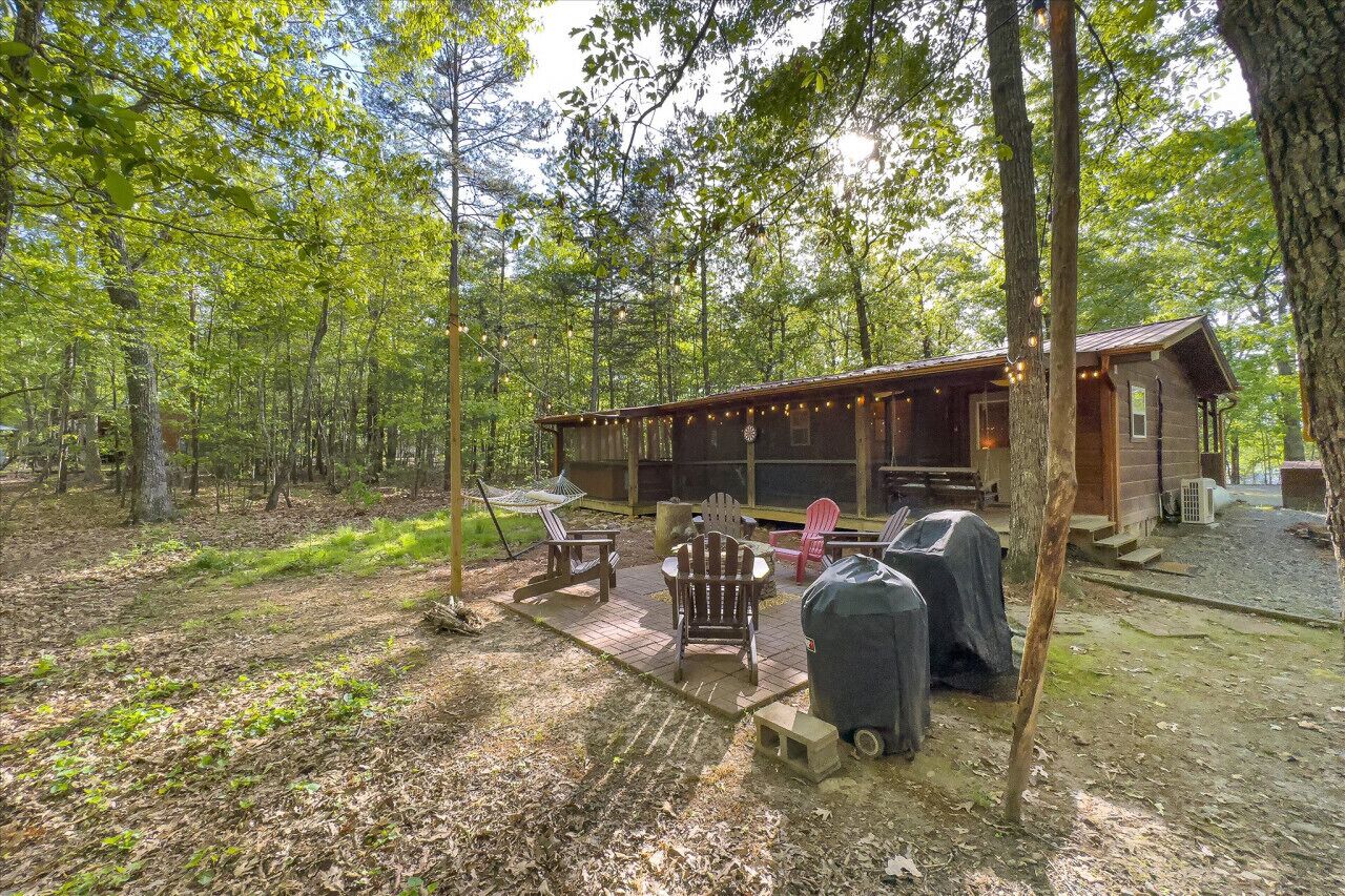 A rustic cabin with a deck, outdoor seating, and a grill area.