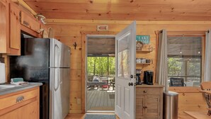 Cocina de cabaña de madera con refrigerador, lavabo y puerta que da a una terraza.