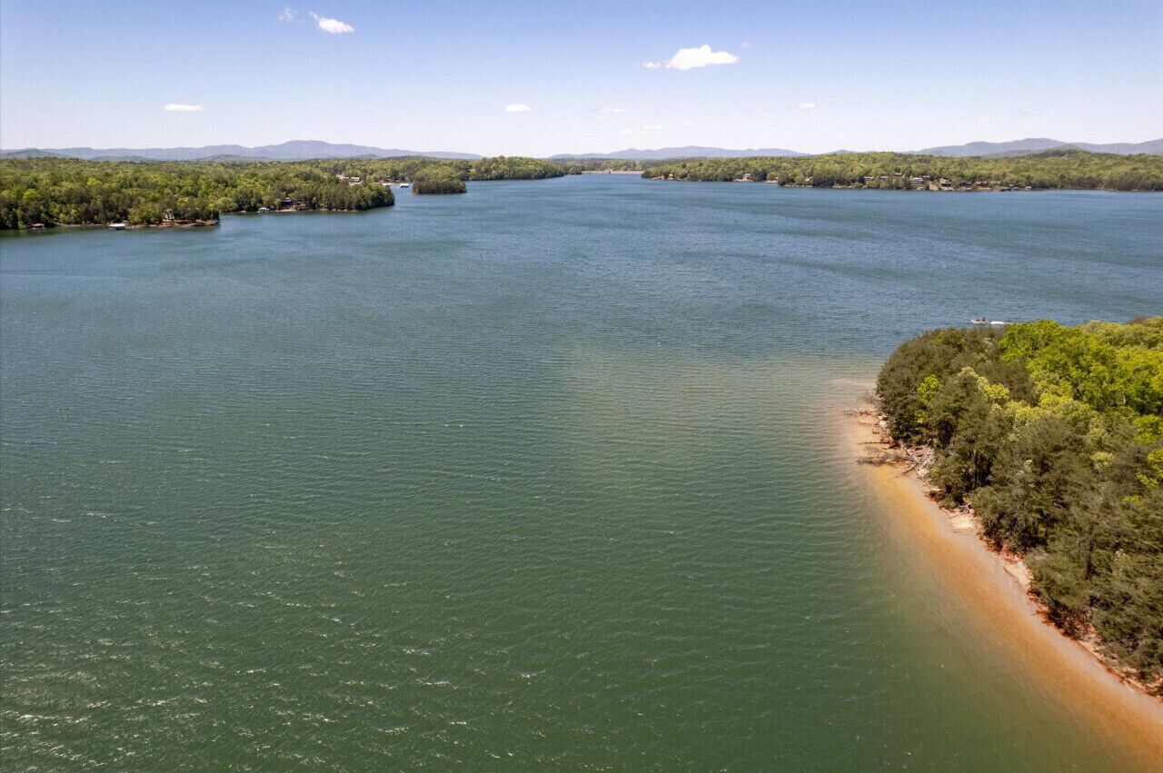 A large body of water with a narrow land strip on the right, surrounded by dense greenery and distant hills.
