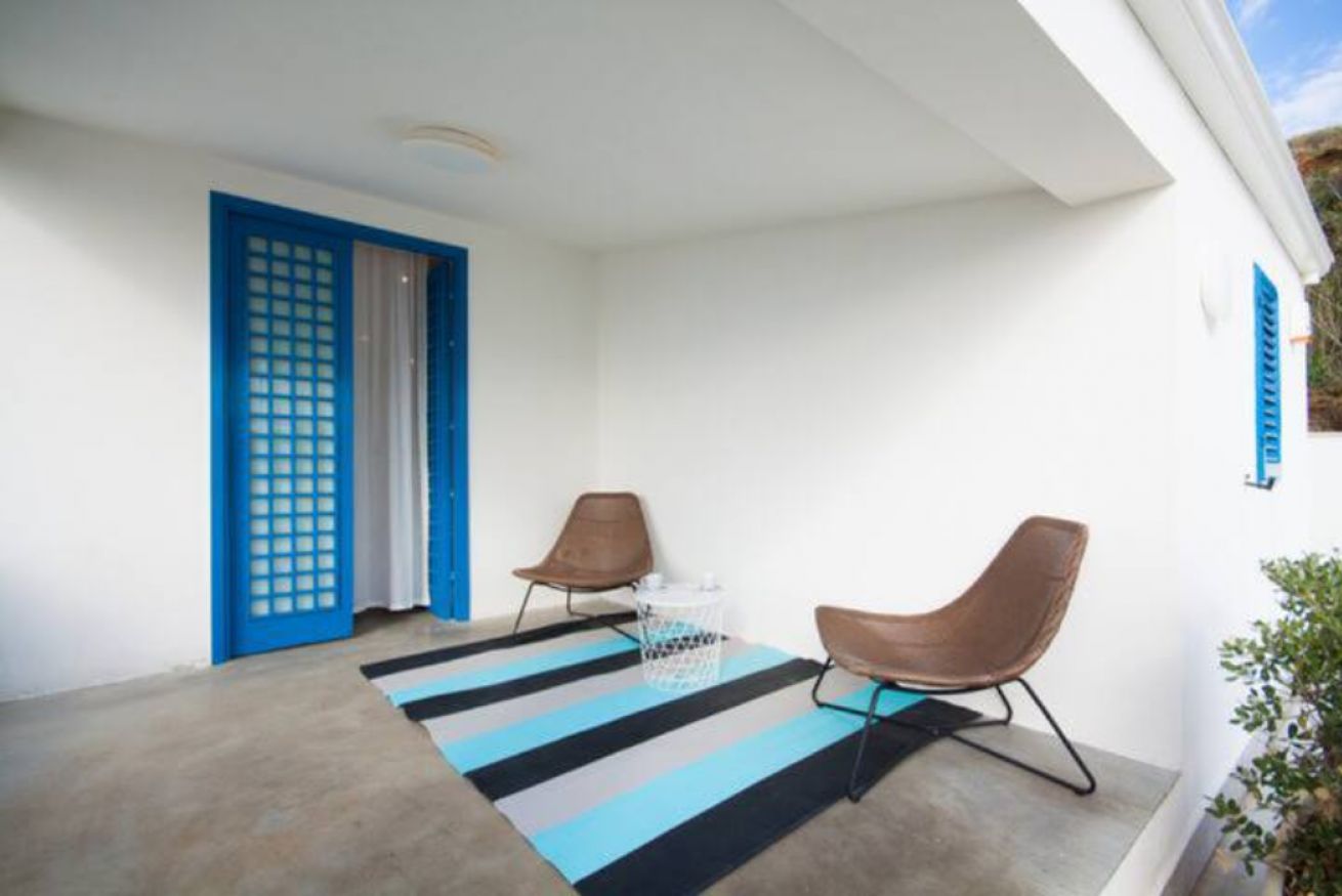 Une pièce avec une porte bleue, deux chaises marron, un tapis à rayures et une poubelle blanche.