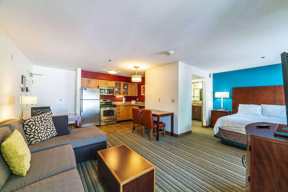 Quarto de hotel com cozinha compacta, cama, sofá e área de jantar.
