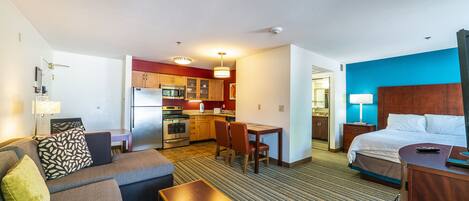 A hotel room with a kitchenette, a bed, a sofa, and a dining area.