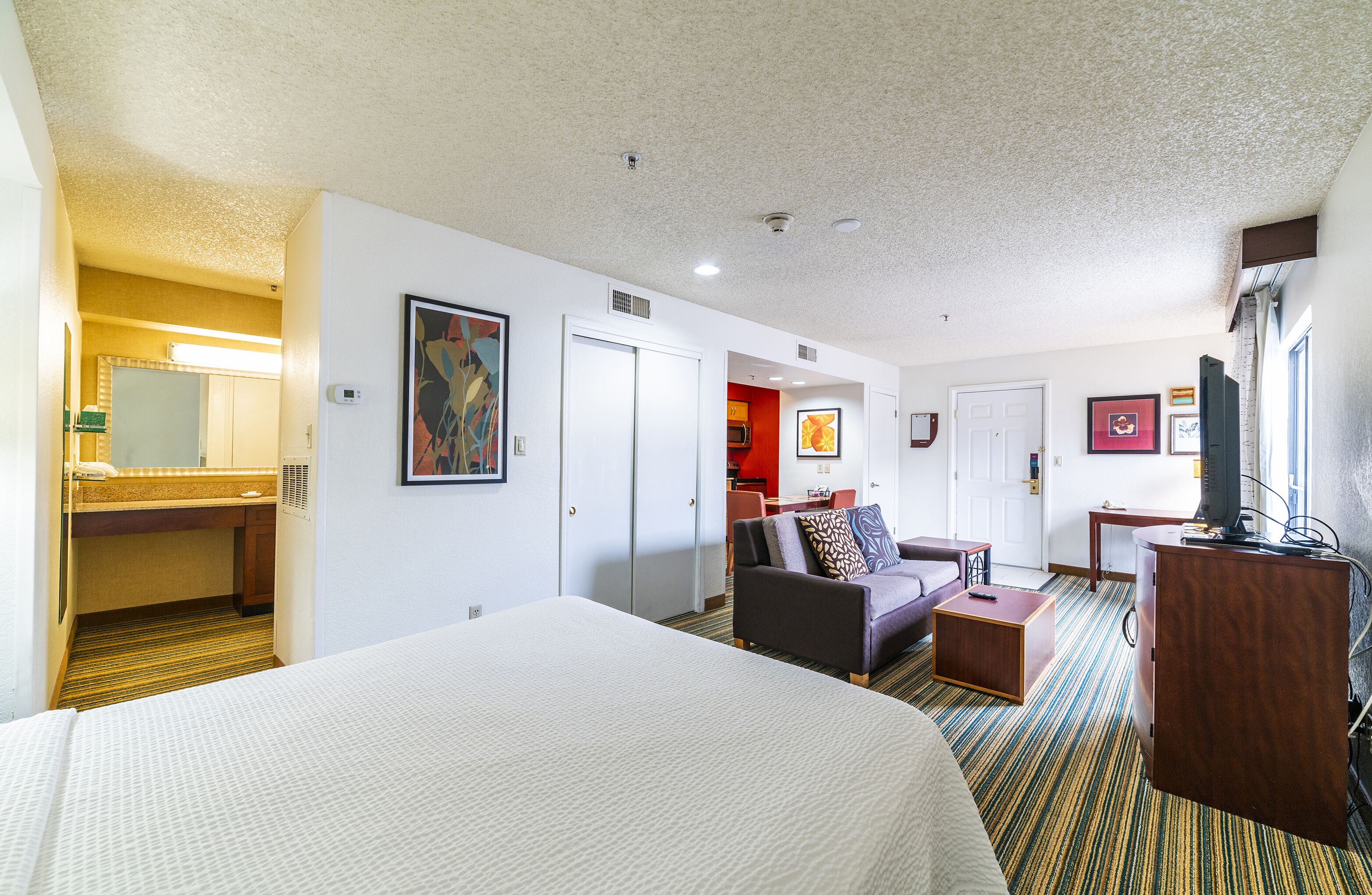 A hotel room with a large bed, a sofa, a desk, and a television.