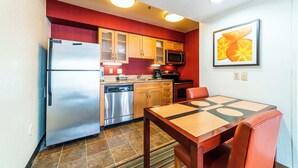 A compact kitchen with a refrigerator, microwave, and dishwasher. There is a dining table with chairs and a rug. - Metro Phoenix Extended Stay (Phoenix)