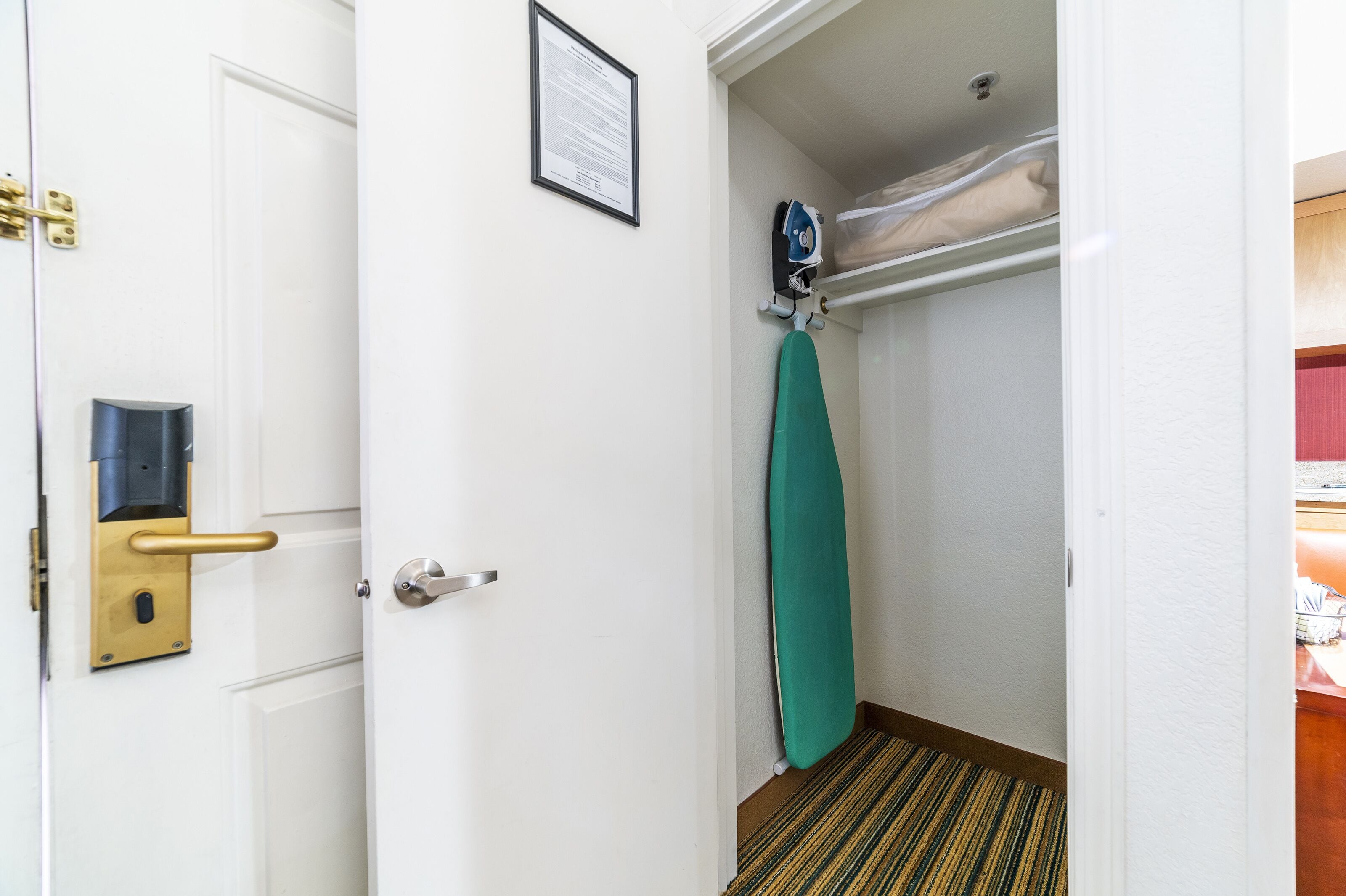A hotel room with a white door, a security card reader, an iron, and a green towel hanging on the wall.