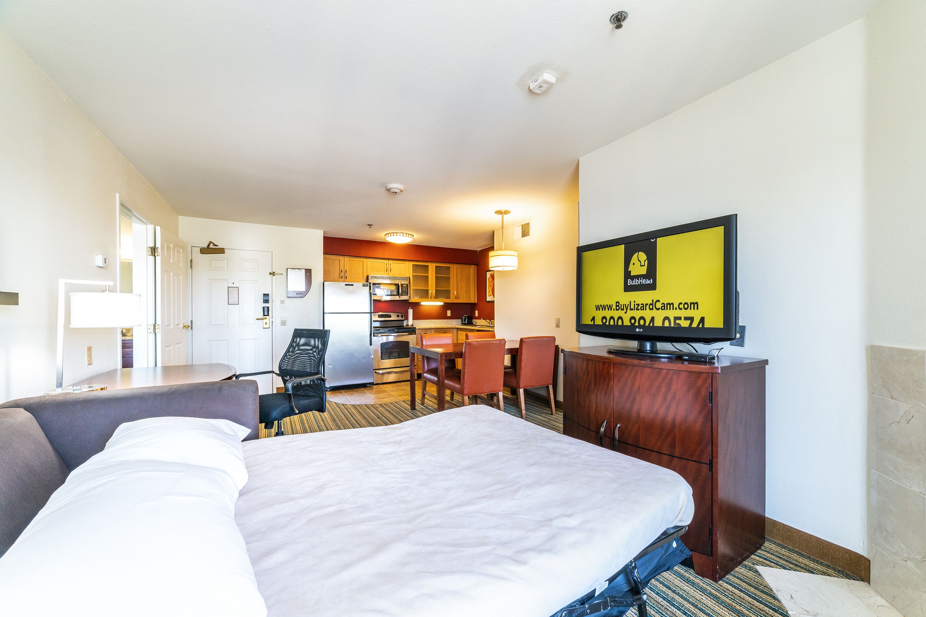 Een hotelkamer met een bed, een bureau, een stoel, een televisie en een kitchenette.