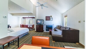 A hotel room with a bed, a sofa, a television, a fireplace, and a ceiling fan. - Metro Phoenix Extended Stay (Phoenix)