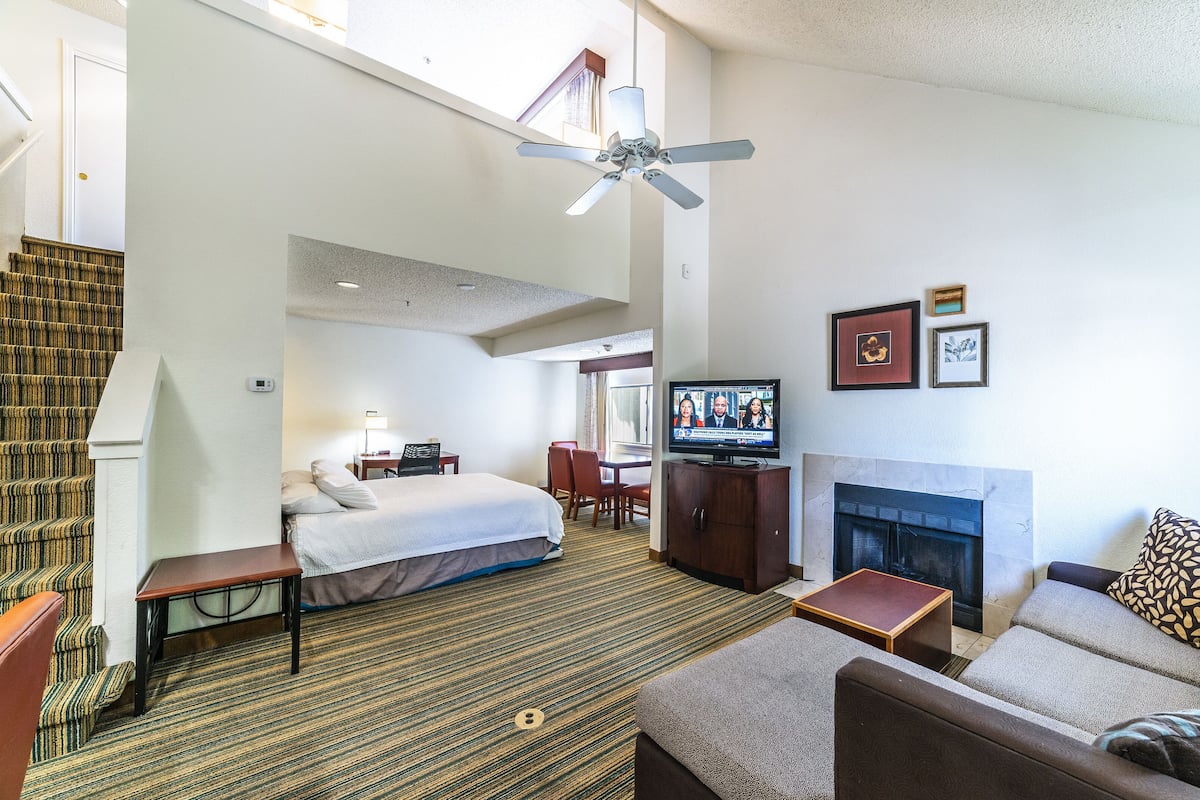 Quarto de hotel com cama, televisão, lareira, ventoinha no teto e escada.